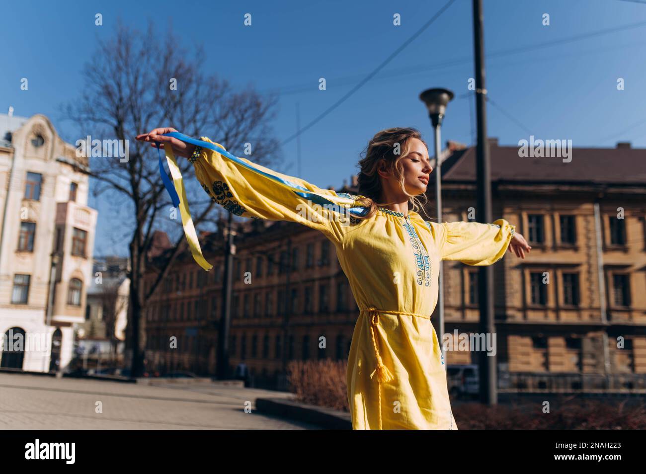 a girl in a yellow Ukrainian dress walks down the street on a sunny day. Independence Day of Ukraine Stock Photo