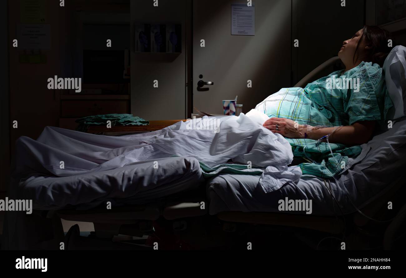 Pregnant woman in labor laying in hospital bed with rays of light on belly stomach at maternity ward Stock Photo
