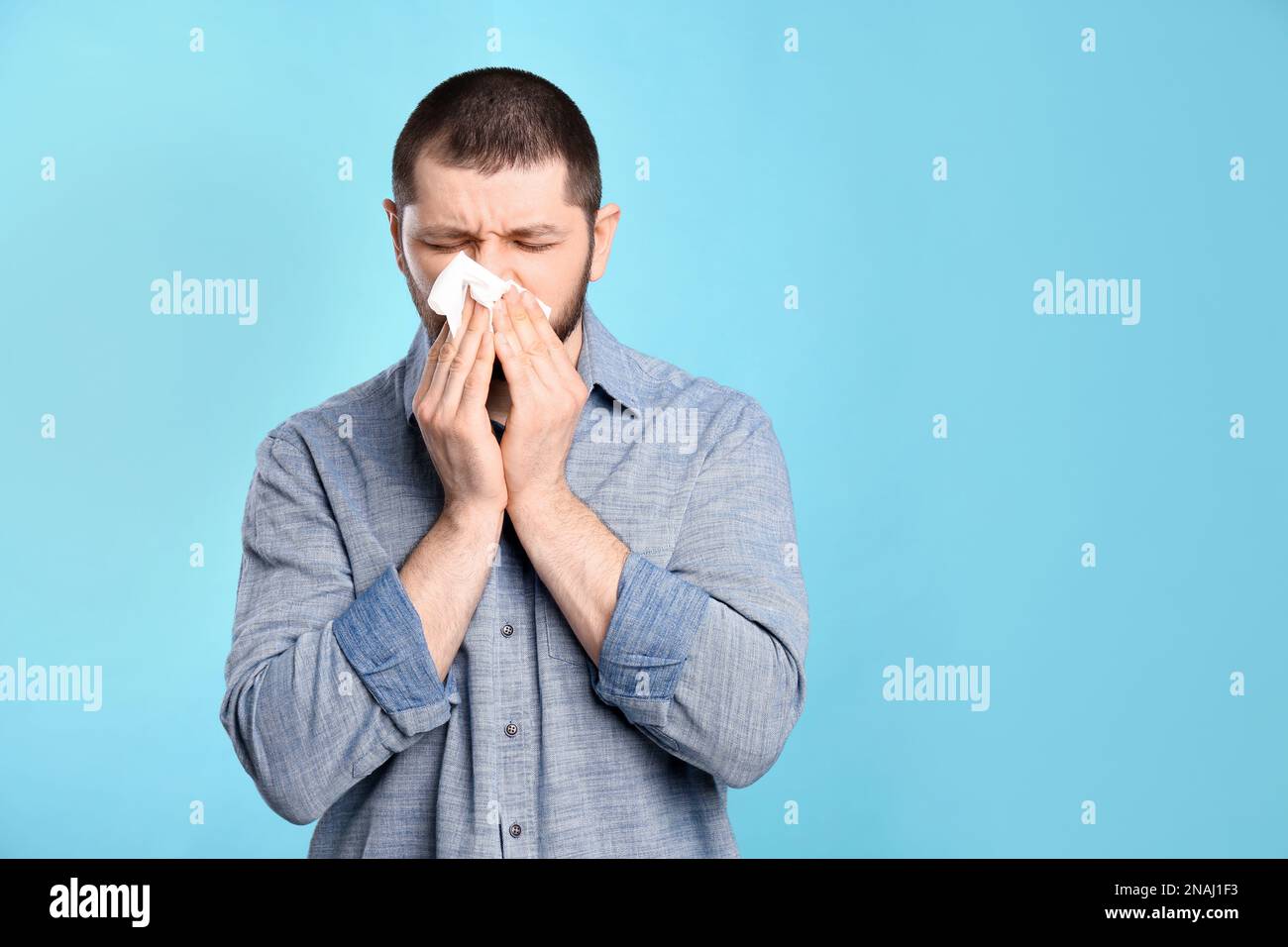 Man with tissue suffering from runny nose on light blue background ...