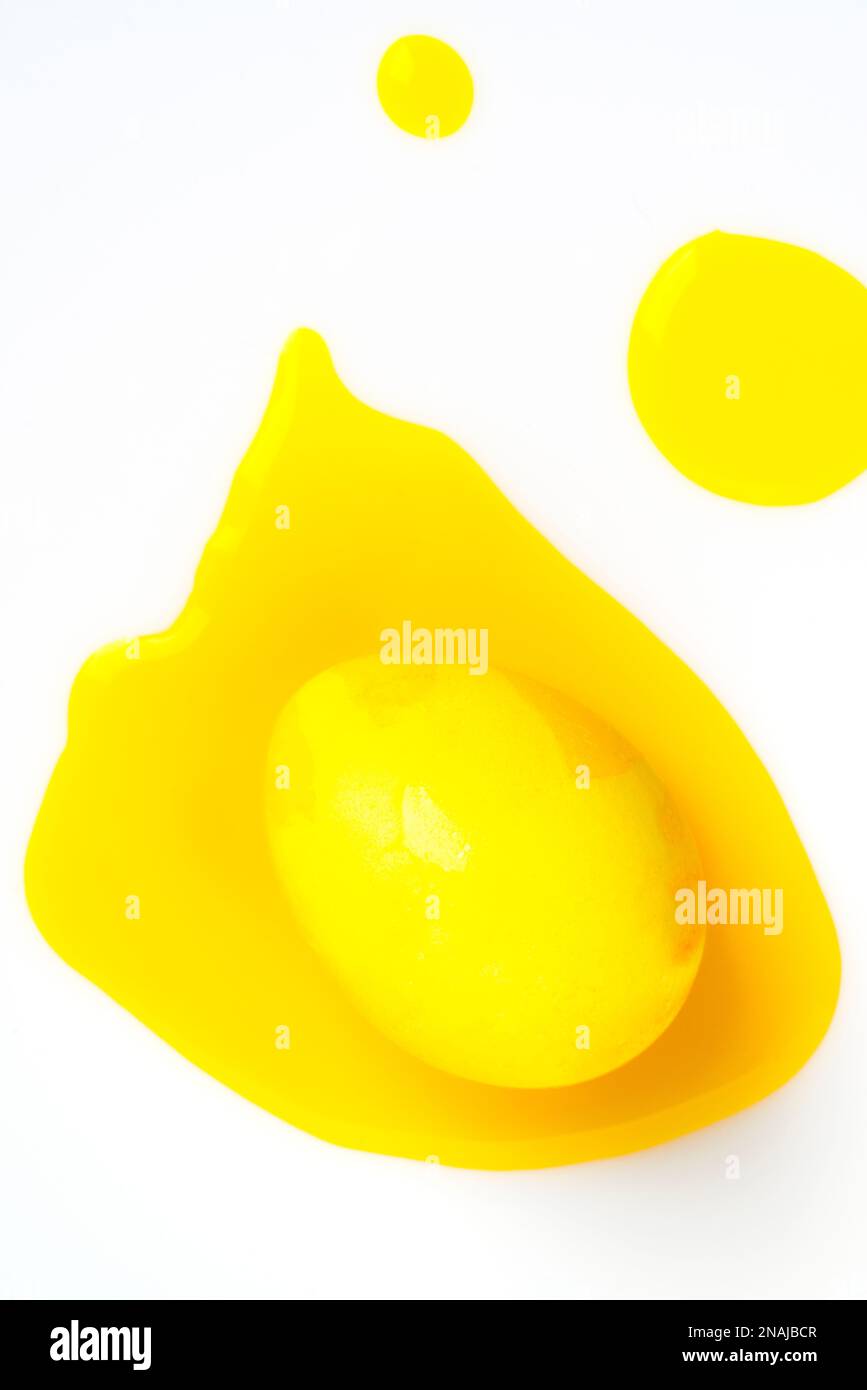 Yellow easter egg and liquid food coloring on white background. Stock Photo