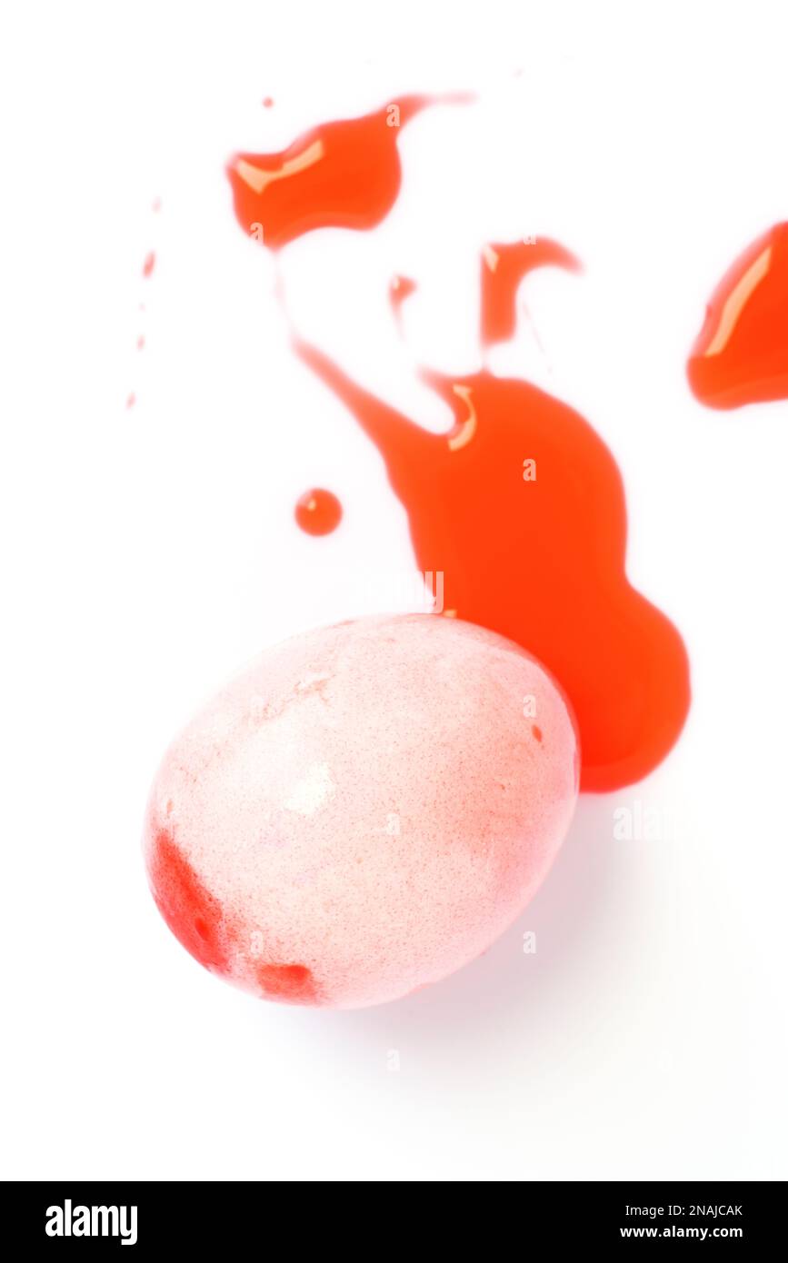 Red easter egg and liquid food coloring on white background. Close up shot. Stock Photo