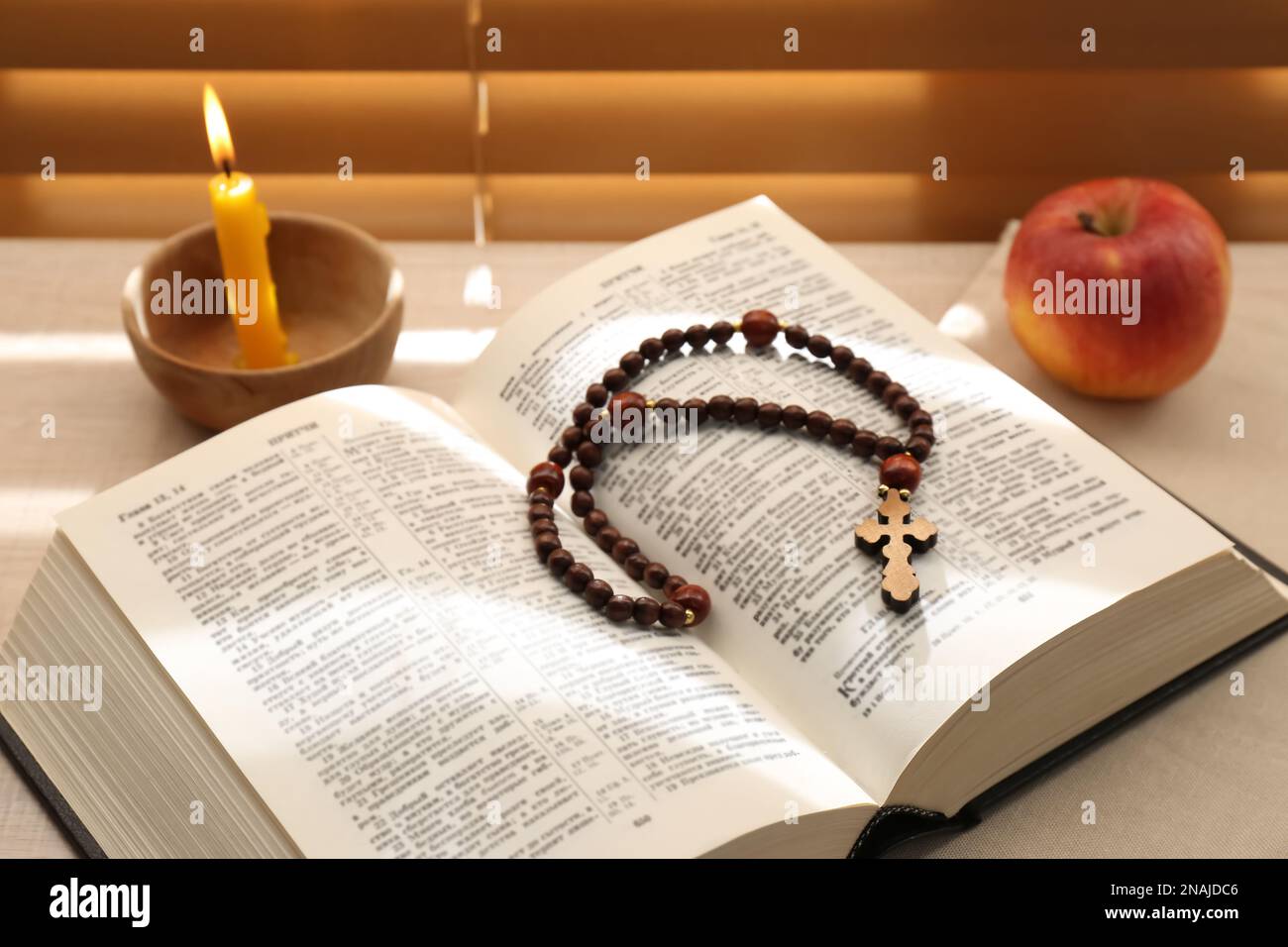 Bible with prayer beads, candle and apple near window indoors. Great ...