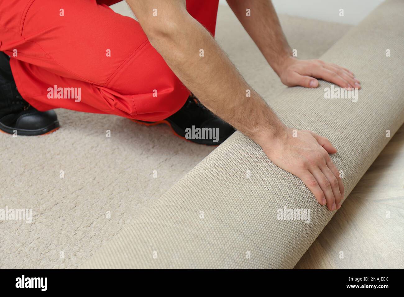 Worker rolling out new carpet flooring indoors, closeup Stock Photo