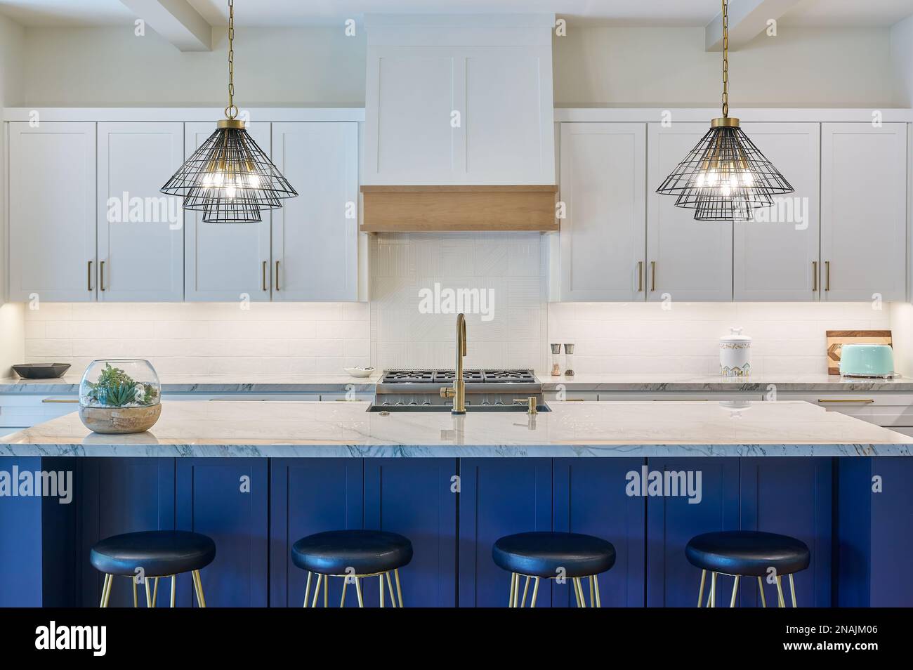 Straight on view of a contemporary kitchen with bar stools, pendant lighting, and cabinetry Stock Photo
