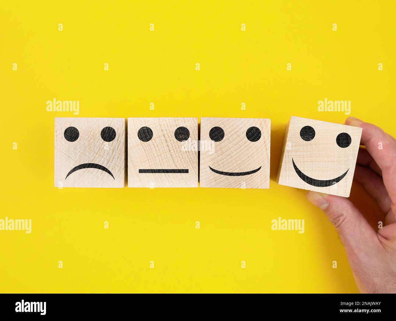directly above view of smiley feedback icons on wooden blocks against yellow background Stock Photo