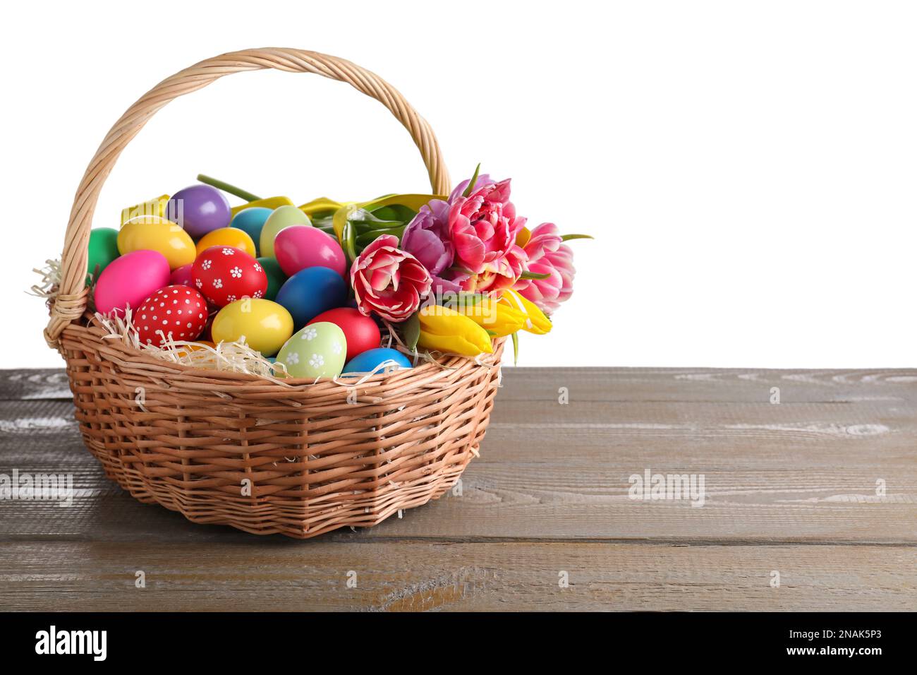 Colorful Easter eggs in wicker basket on wooden table against white ...