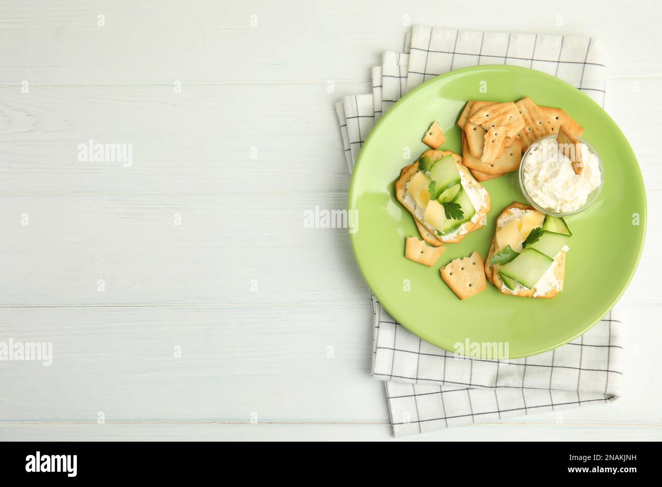 Delicious crackers with cream cheese, cucumber and parsley on white