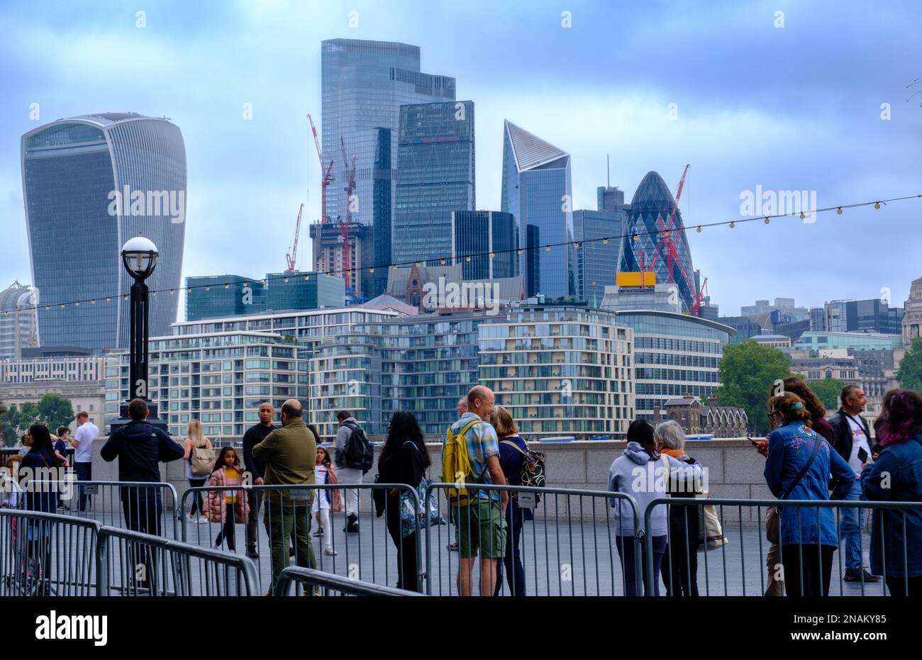 People on Queens Walk across River Thames from iconic London skyline including Gherkin, Walkie Talkie, The Scalpel & Cheese Grater, City of London. Stock Photo