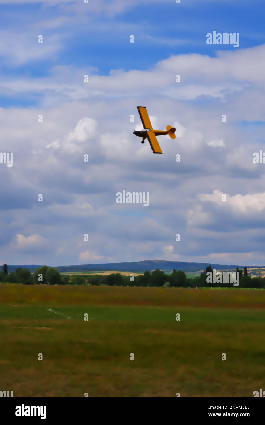 Yellow single engine airplane maneuvering close to the ground with cloudy sky at the background Stock Photo