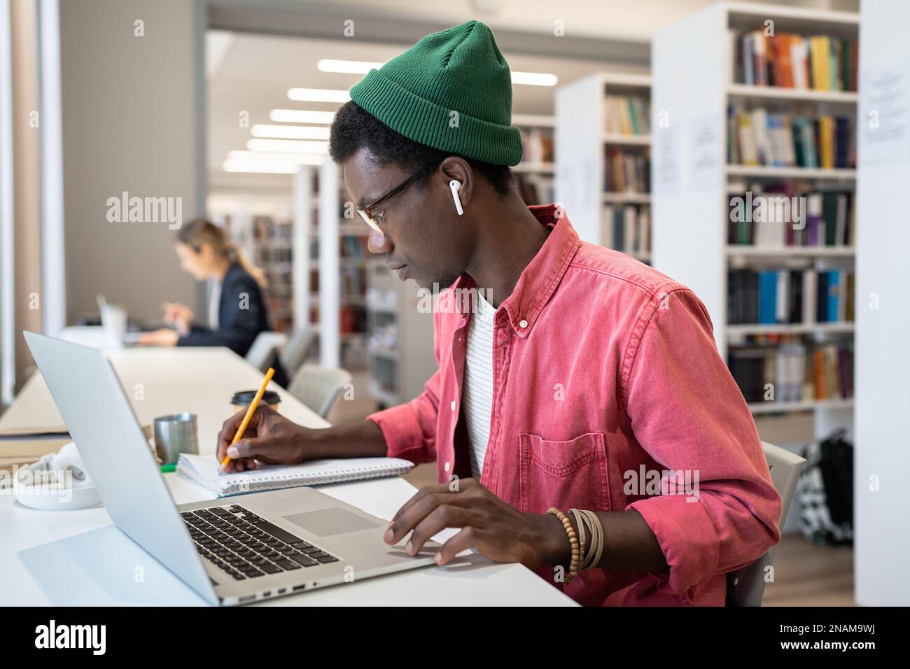Focused African guy online student taking notes during webinar, studying in library on laptop Stock Photo