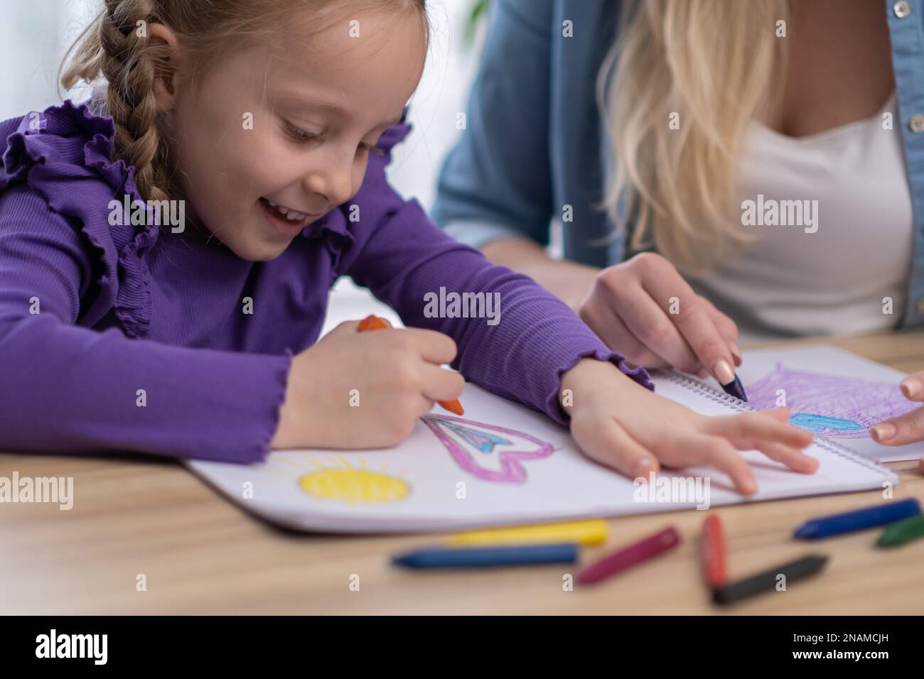 Close up little girl painting with mom using different colours pensil