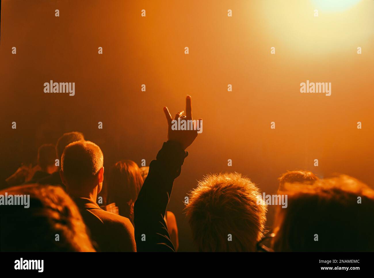 Man in crowd raising hand with devil horns in orange spotlight at a live rock concert Stock Photo