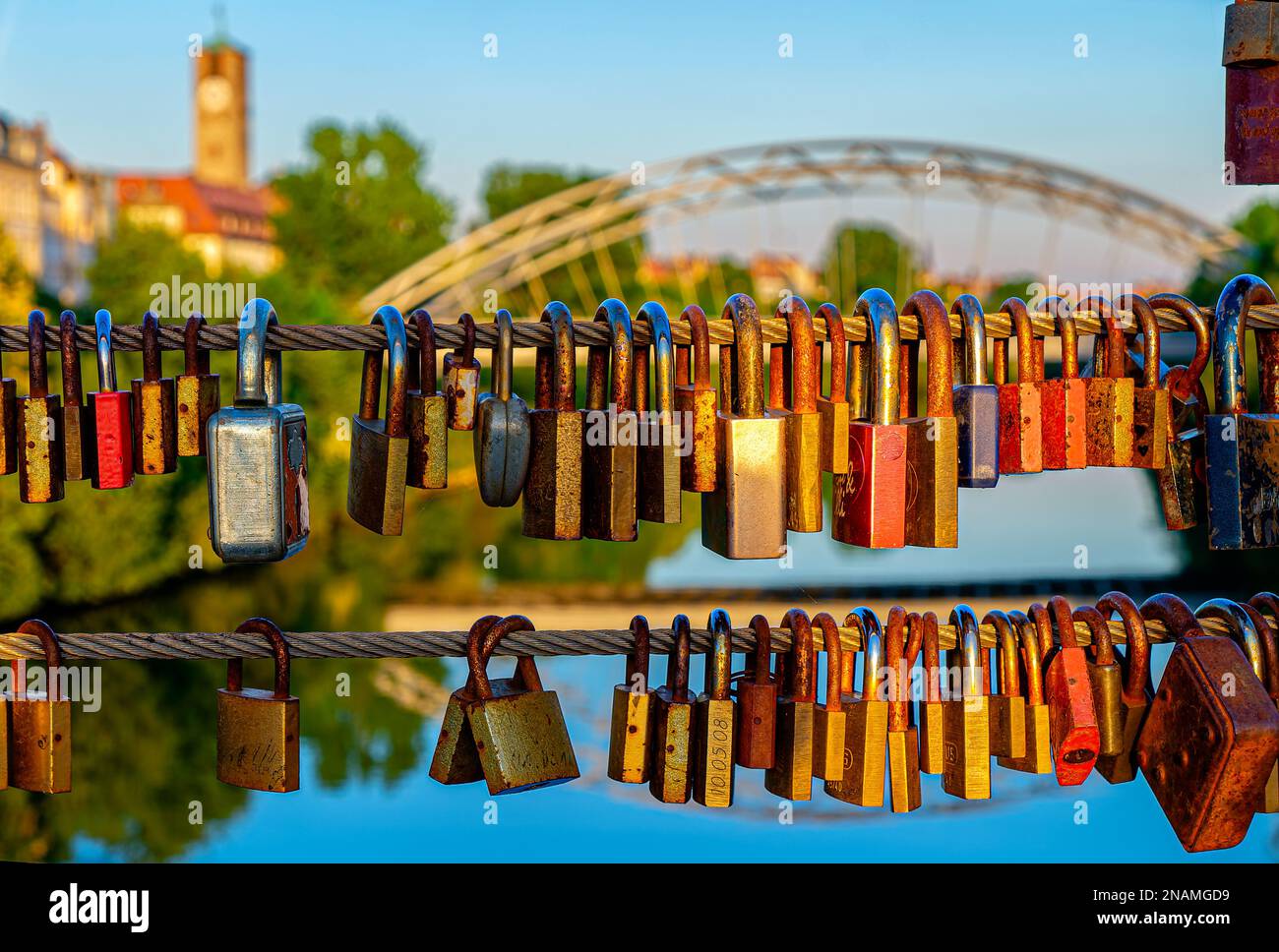 Love locks on wire cable romantic ritual in front of Luitpold bridge and Church of the Redeemer during sunset in Bamberg Germany Stock Photo