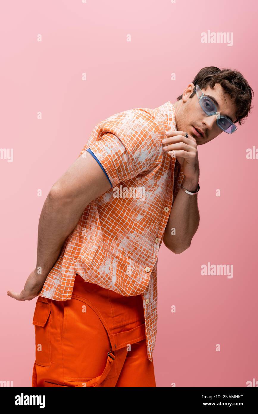 Stylish model in orange overalls and blue sunglasses looking away isolated on pink,stock image Stock Photo