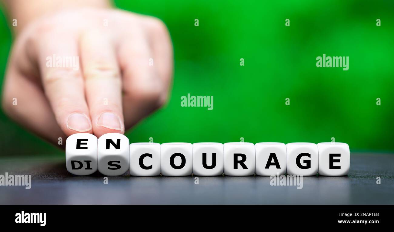 Hand turns dice and changes the word discourage to encourage. Stock Photo