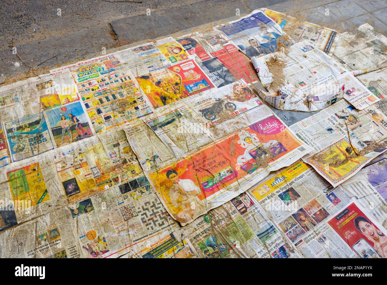 Colourful local newspaper pages laid out on a pavement in Fariapukur