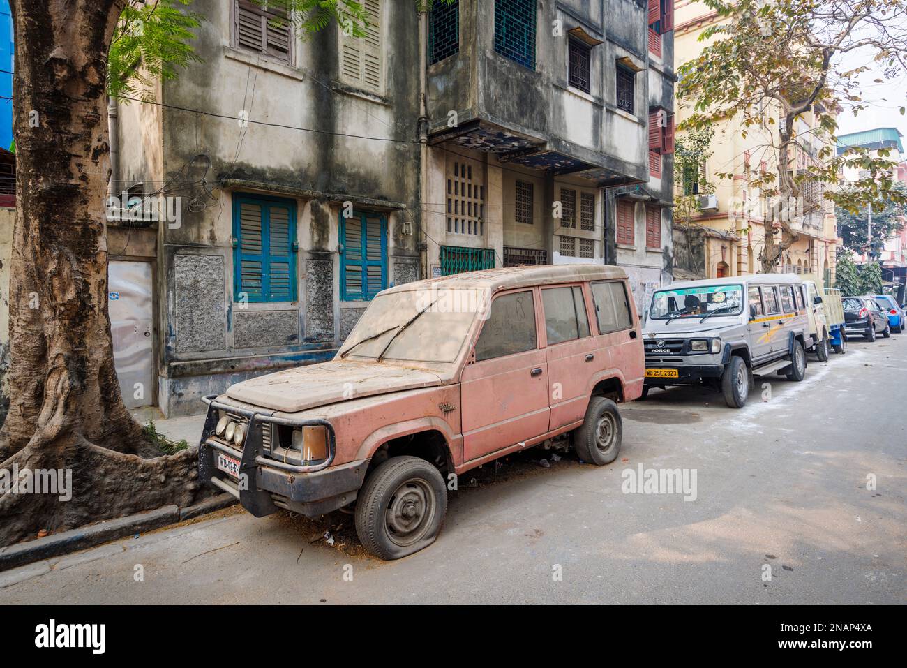 A rusty battered old car or van (a Tata Sumo) parked in the street in