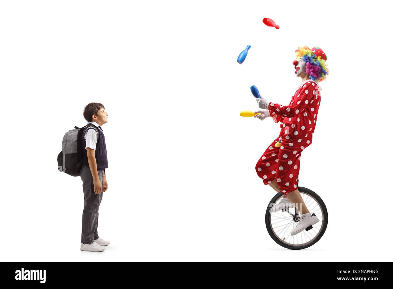 Full length shot of a schoolboy looking at a clown juggling and riding ...