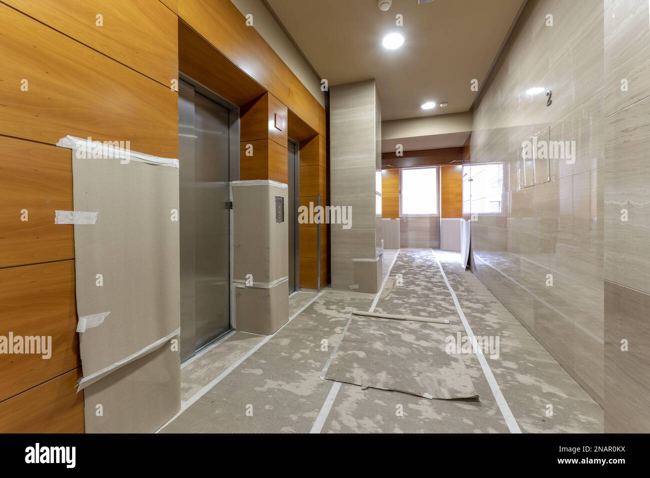 Elevator area of an office building with wooden and marble walls with cardboard-covered floors due to being under renovation Stock Photo