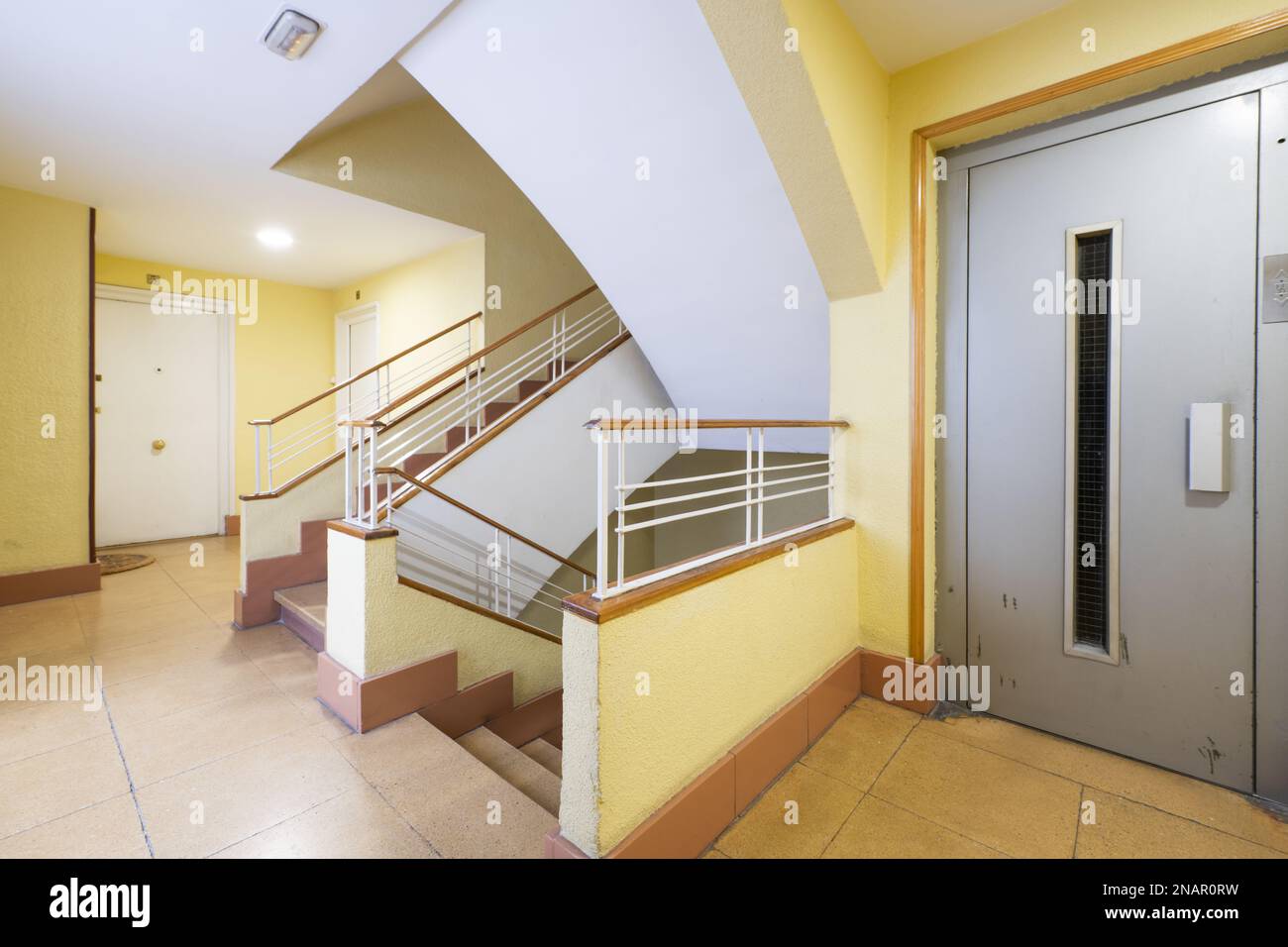 Elevator area of an old residential building with central stairs with white metal and wooden railings Stock Photo