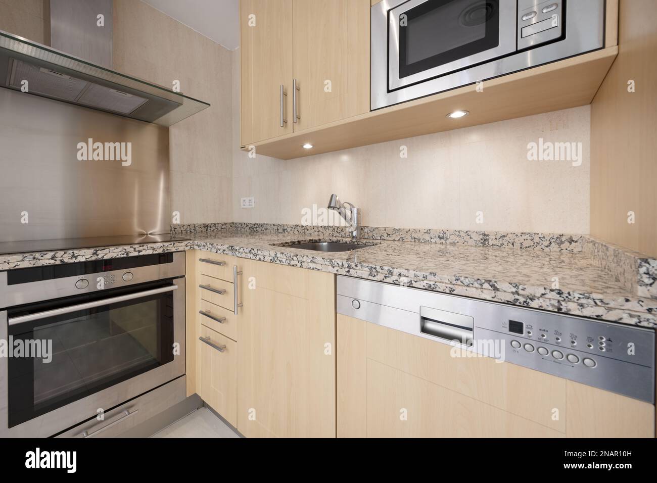 Corner of a newly installed modern kitchen with pink granite worktops, light wood cabinets, panel-integrated stainless steel appliances and courtesy l Stock Photo