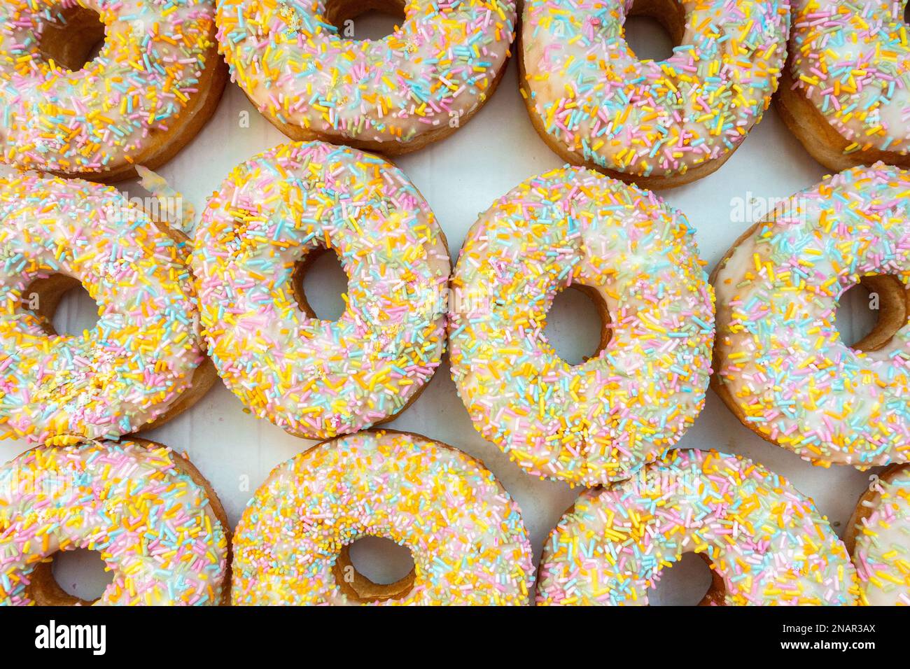 A box of glazed ring doughnuts with white frosting and colourful