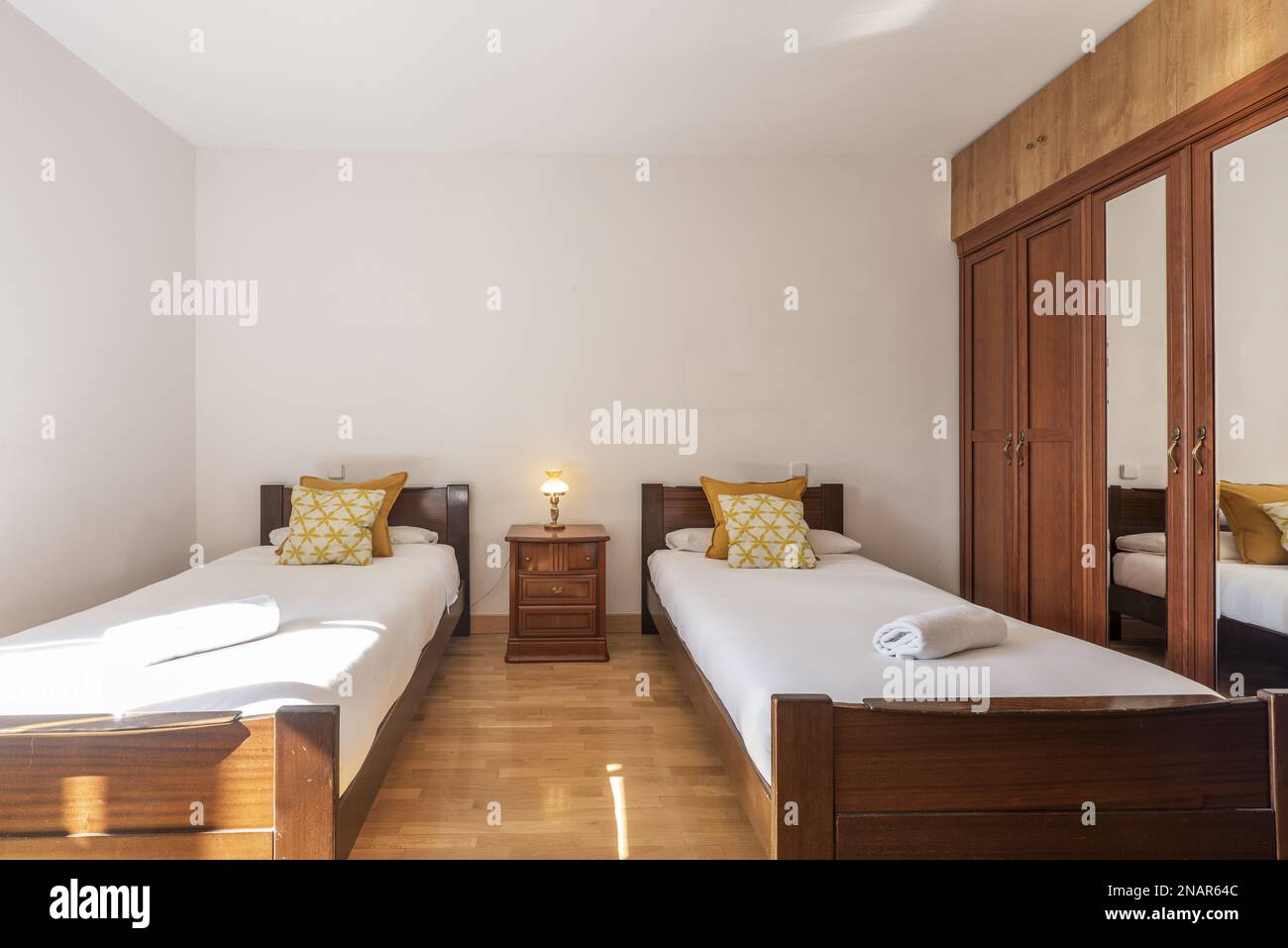 A bedroom with matching wooden single beds with a builtin wardrobe with central mirror doors