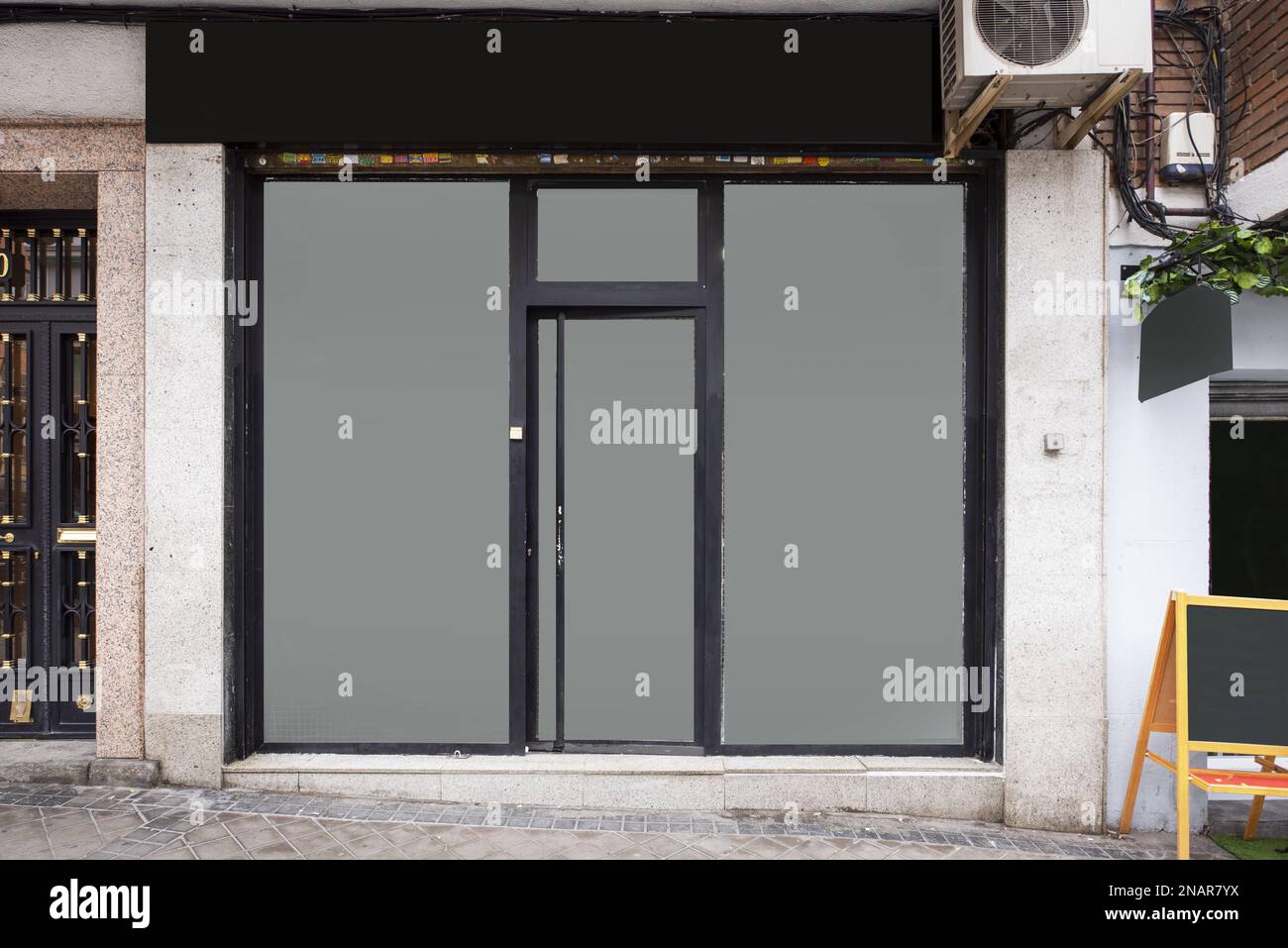 Front of a small street level shop with black metal trim and opaque glass surfaces Stock Photo
