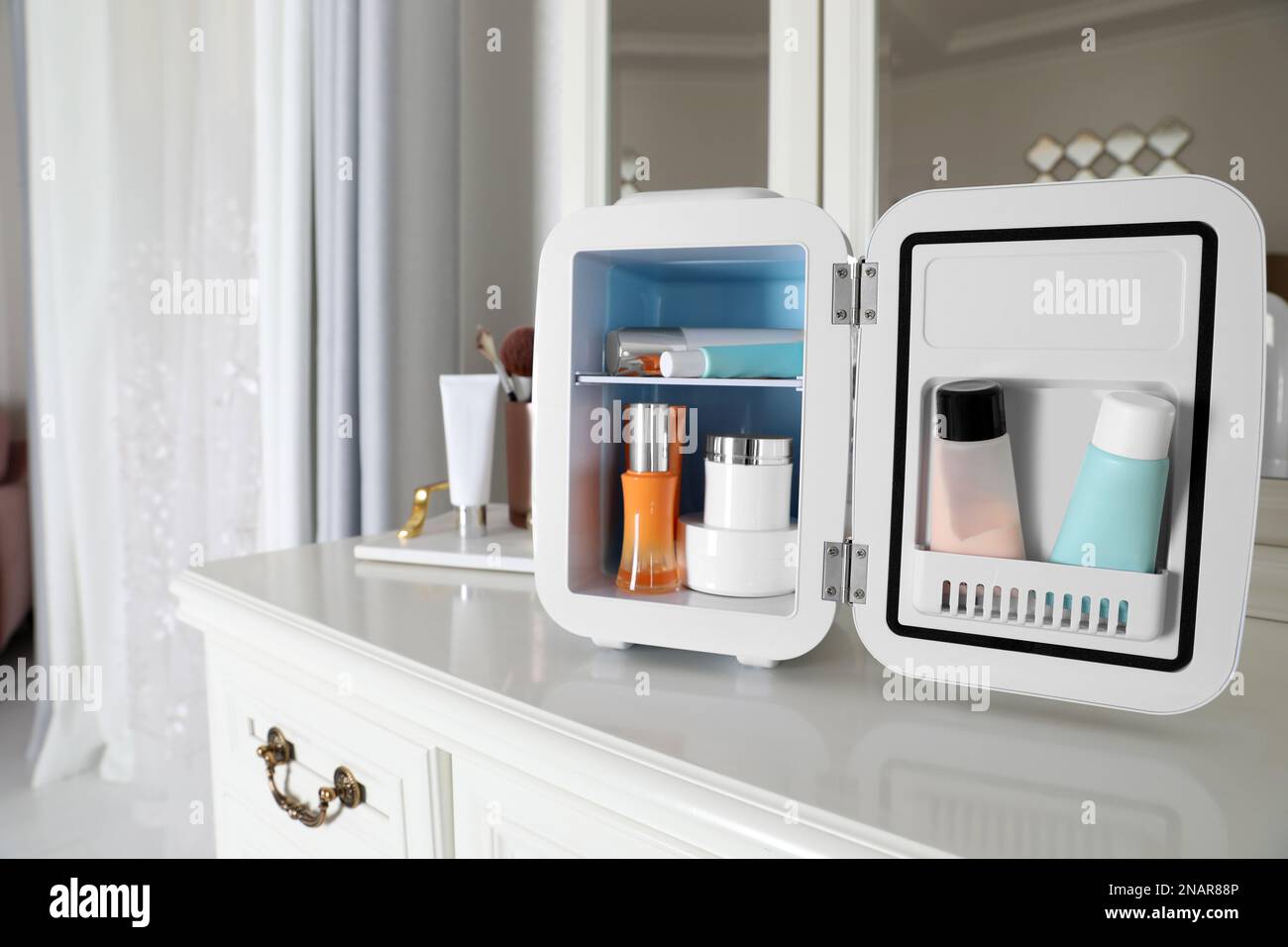 Mini fridge with cosmetic products on white vanity table Stock Photo
