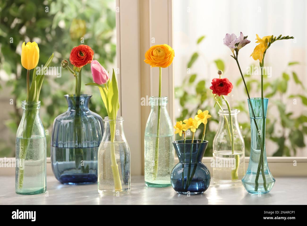Different beautiful spring flowers in glassware on window sill Stock ...