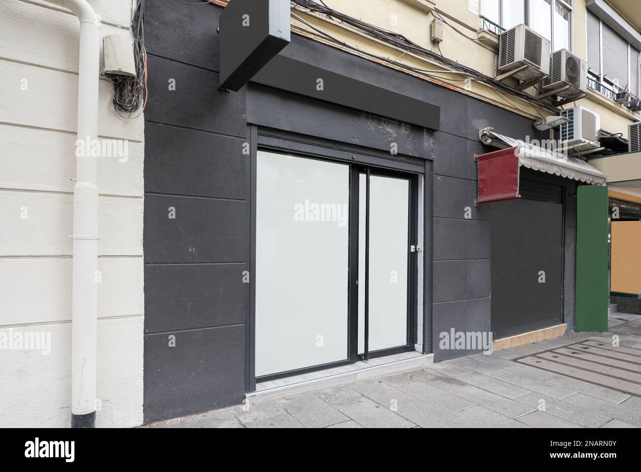Local at street level in an old building with a black painted facade, opaque windows and metal shutter closure Stock Photo
