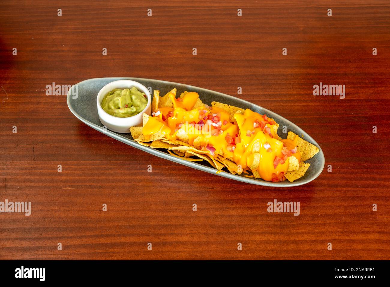 An elongated tray with nachos with melted cheese, pico de gallo and a small bowl of guacamole Stock Photo