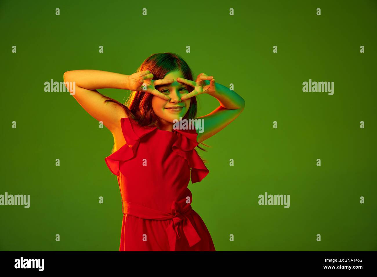 Positive vibe, good mood. Little girl, child in red outfit posing over green studio background