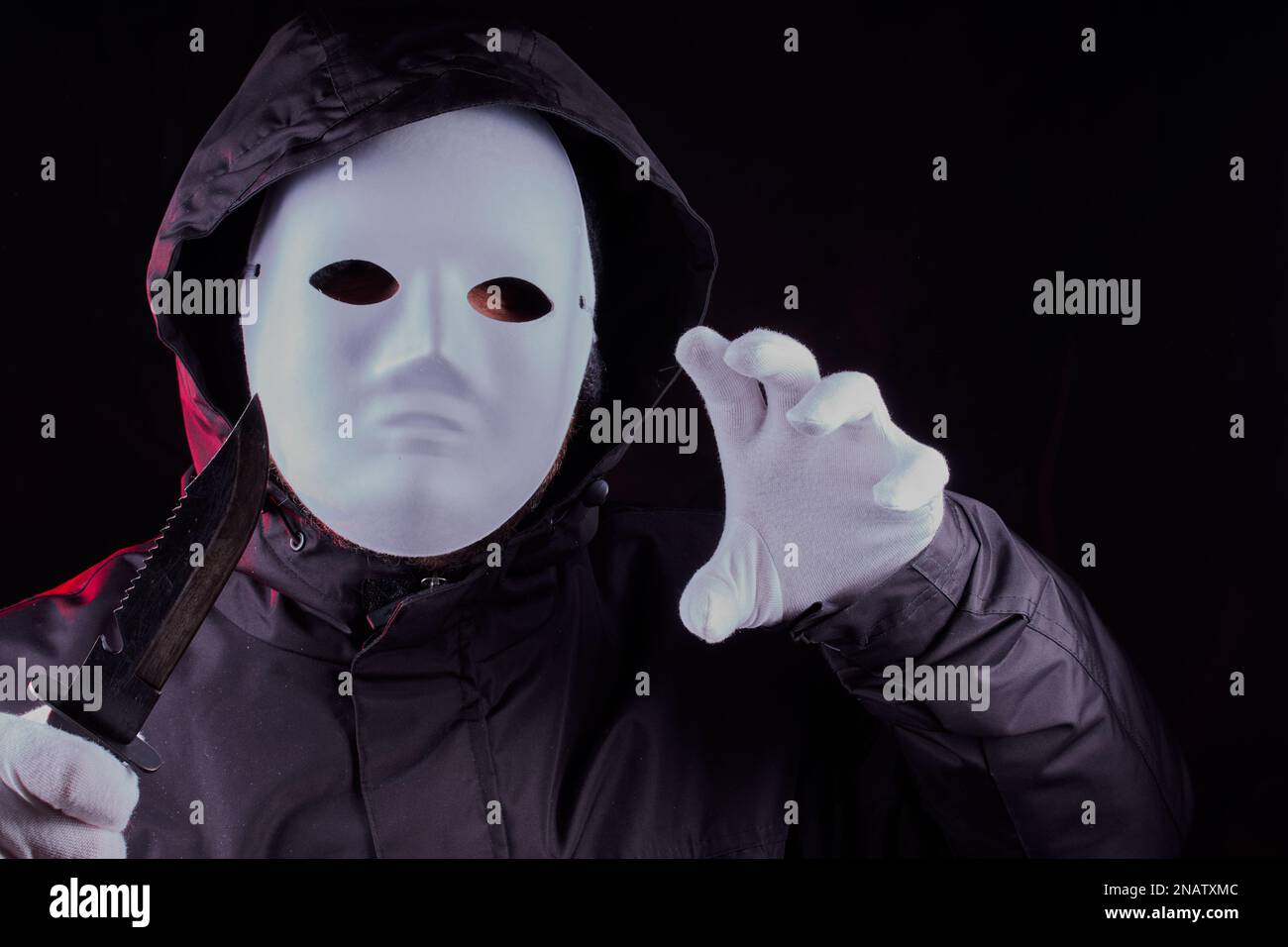 Masked person with black hooded jacket on and holding a knife in a threatening manner. Stock Photo