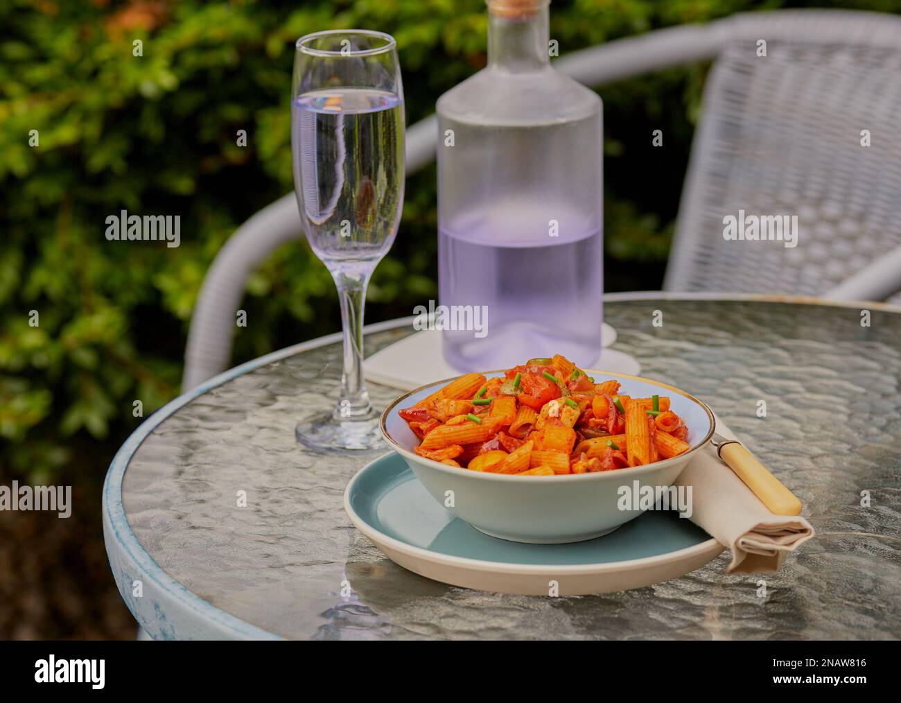 Summer pasta dish outside on a garden table with some drinks, with some greenery in the background. Stock Photo