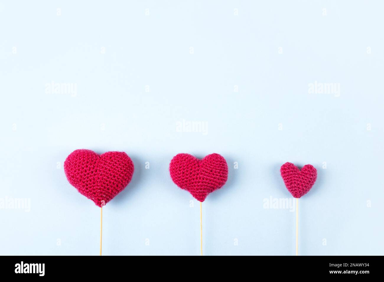 Three knitted red hearts on a blue background with space for text. Valentine's day concept, holiday card. Bouquet of hearts. Stock Photo