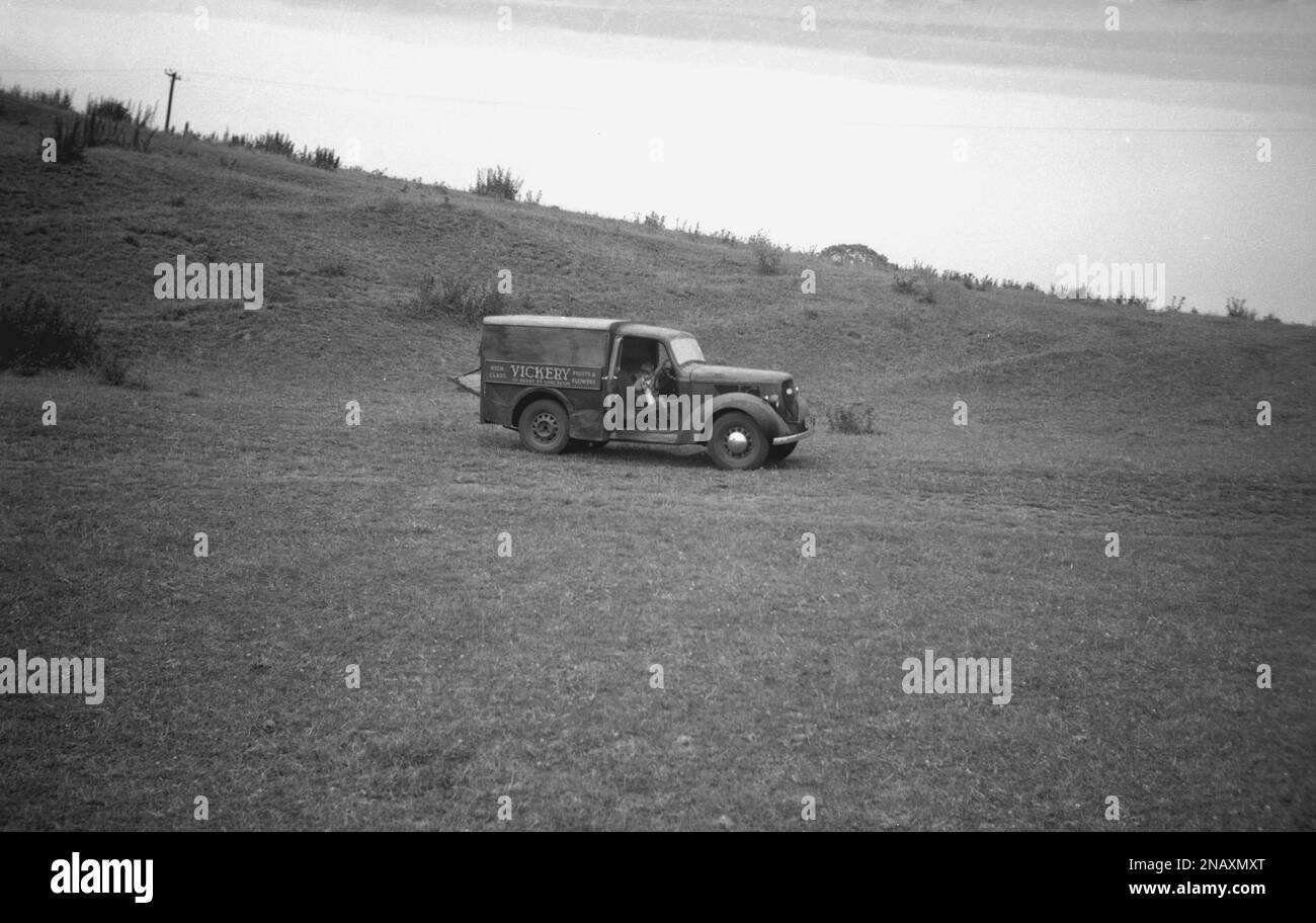 1950s, historical, outside in the middle of a hillside field, a small boy sitting in the front seat of a small delivery van of the era, England, UK. Name on the side of the van, Vickery, Fruits & Flowers, of Derby & Long Eaton. Stock Photo