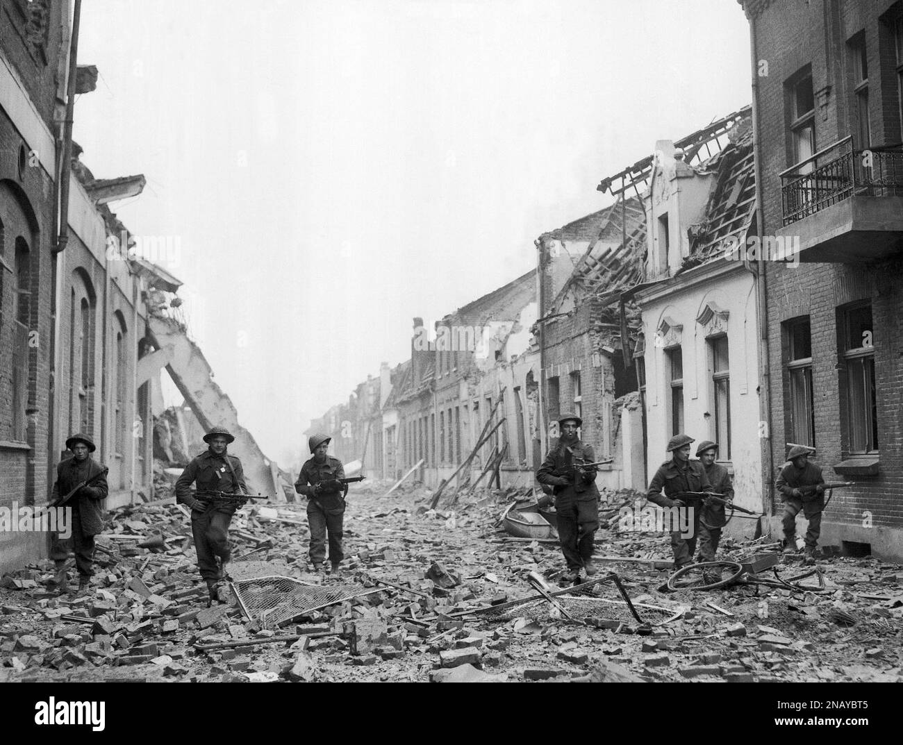 British infantry cautiously advance along a street strewn with wreckage ...