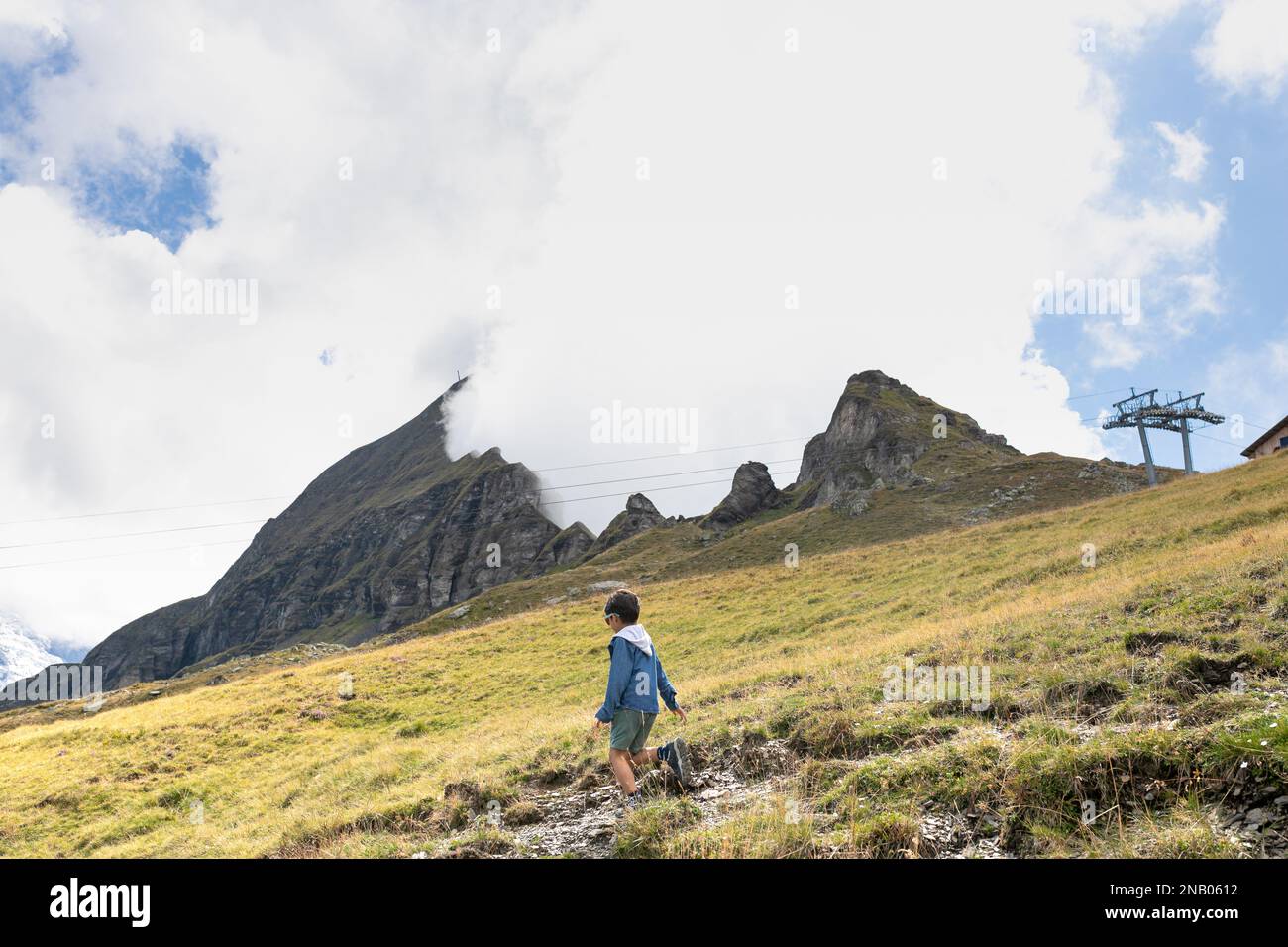 Hike trail from Mannlichen to Wengen, Switzerland alps, scene of giant cloud falling in a valley, opening mouth of the mountain. Young child walking. Stock Photo