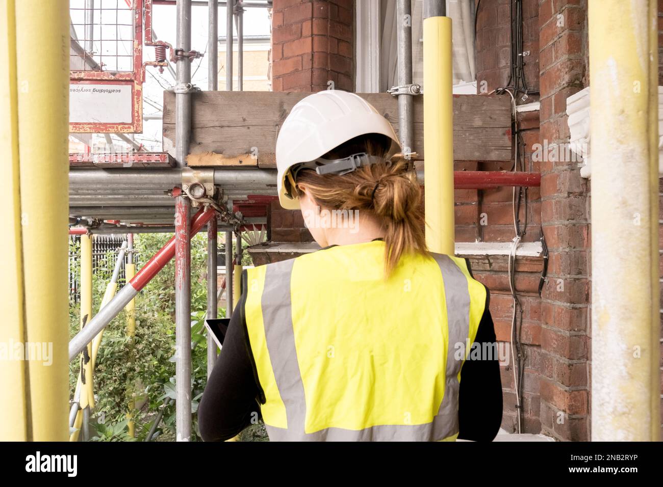 Female chartered civil engineer working in a construction site building, taking notes on her tablet, condition inspection survey, hard hat and yellow Stock Photo