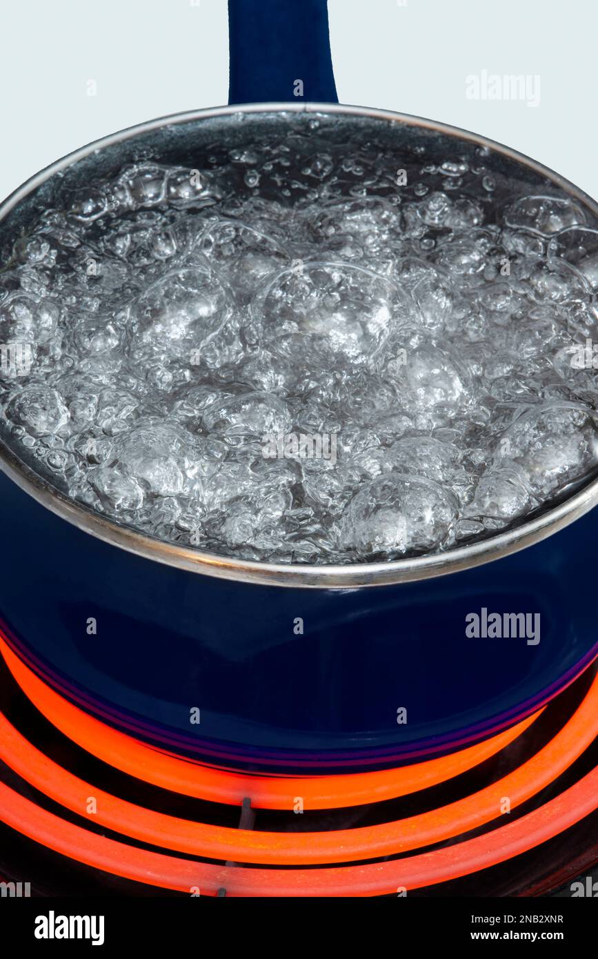 Vertical close-up shot of a blue pot on a stove top on a red hot burner holding boiling water. Stock Photo