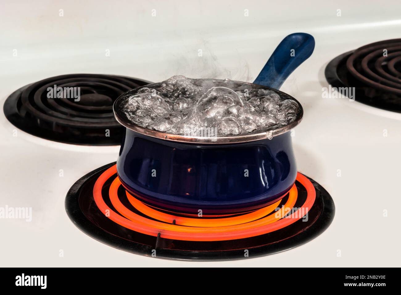 Horizontal shot of a blue pot on a stove top on a red hot burner holding boiling water.  Copy space. Stock Photo