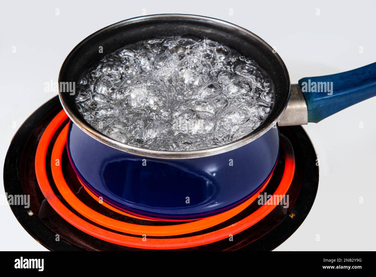 Horizontal shot of a blue pot on a stove top on a red hot burner holding water at a hard rolling boil.  Copy space. Stock Photo