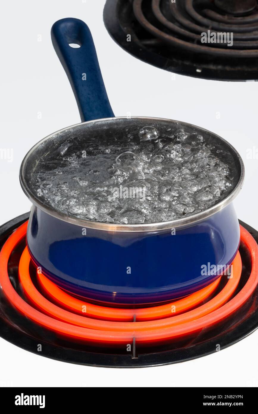 Vertical shot of a blue pot on a stove top on a red hot burner holding boiling water.  Copy space. Stock Photo