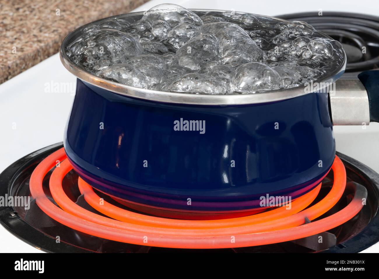 Horizontal shot of a blue pot on a stove top on a red hot burner holding boiling water. Stock Photo