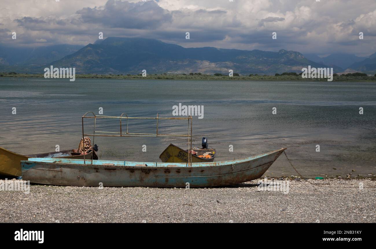 The old fishing boats at the beach of the Shkodra Lake in the spring with peaks in the background, Albania Stock Photo