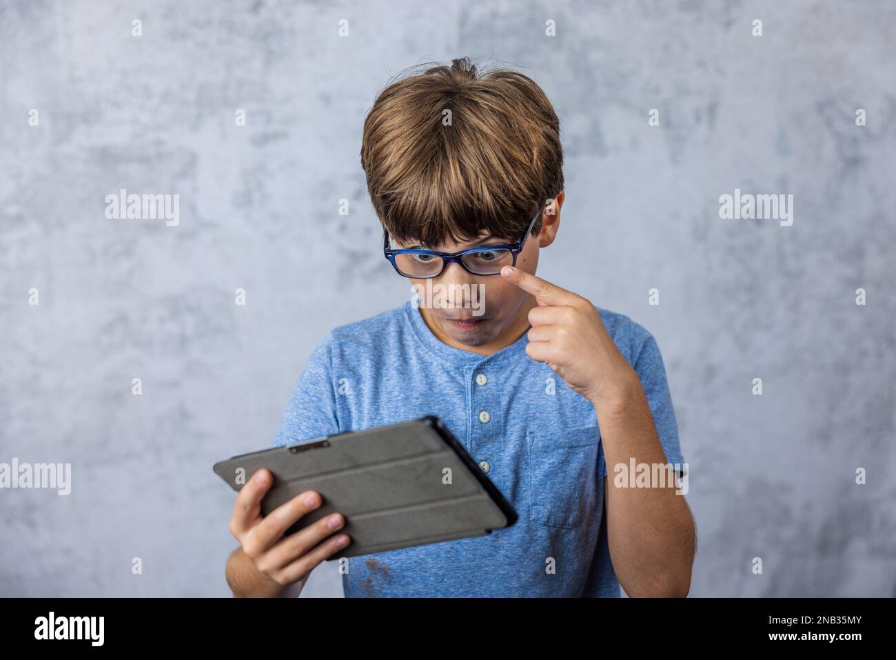 A little caucadian boy with glasses playing with his electronics tablet for screen time with copy space Stock Photo