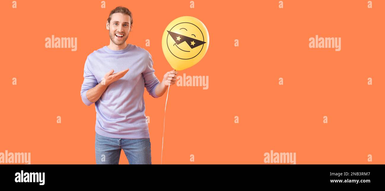 Handsome young man and balloon with drawn emoticon on orange background with space for text Stock Photo