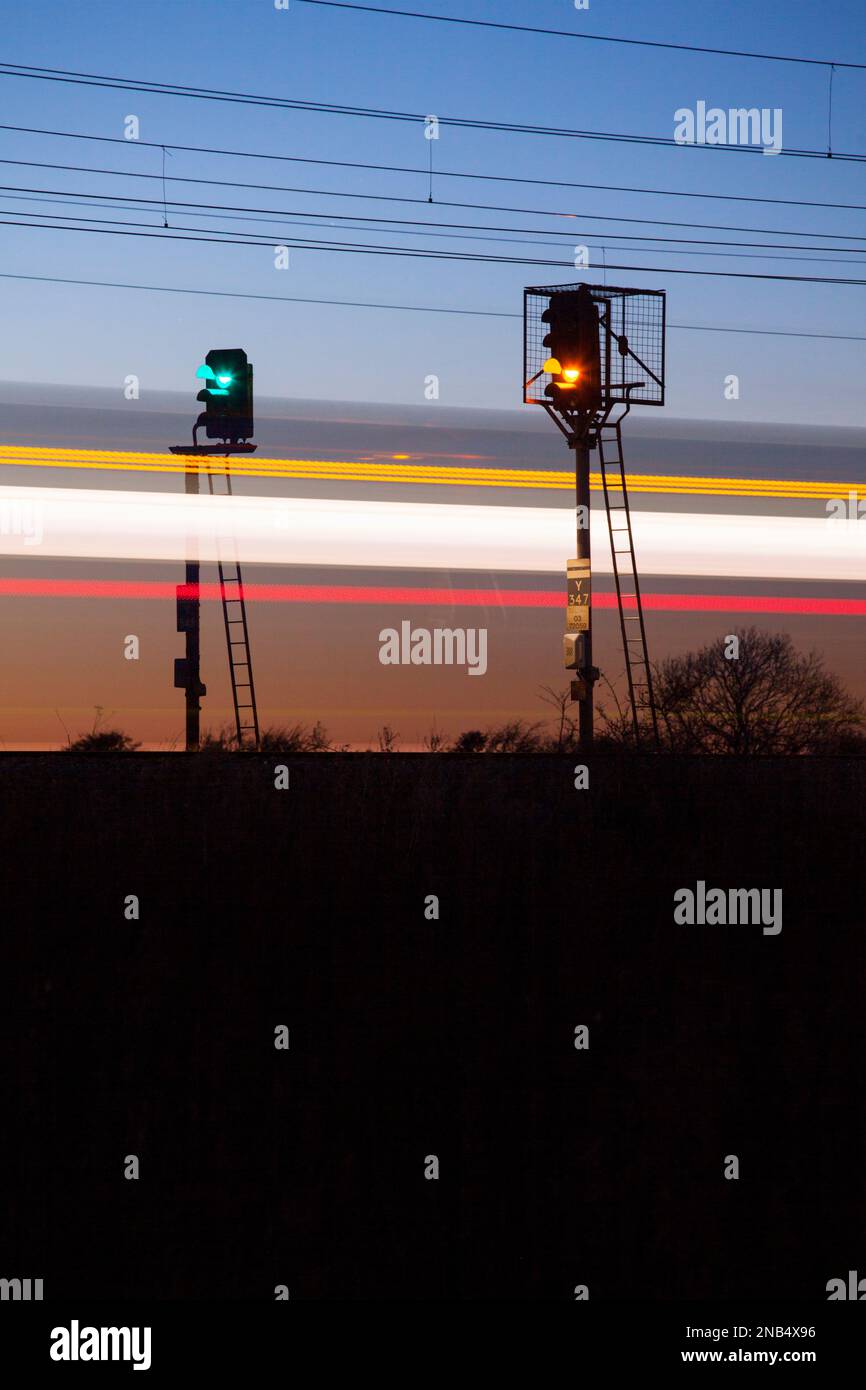 LNER train passing 4 and 3 aspect colour light railway signals  at sunset signals Y347 (R) Y345 (L) at Newton On Ouse leaving a light trail Stock Photo