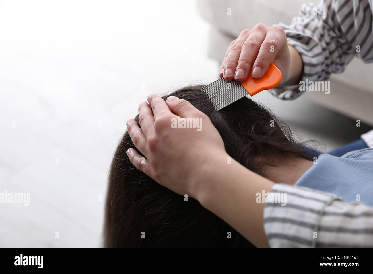 Mother using nit comb on her daughter's hair indoors. Anti lice